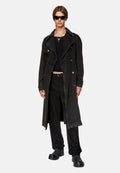 Schwarzer Denim-Trenchcoat mit großen Revers und doppelter Knopfleiste. Getragen über einem schwarzen Oberteil und Hose, ergänzt durch klobige Schuhe.