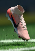 Rosa und weiße Nike Fußballschuhe mit schwarzem Swoosh, die Gras auf einem grünen Feld mit weißen Linien markieren.