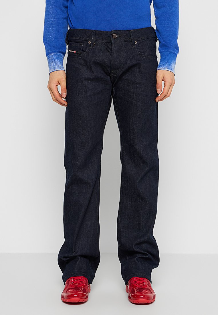 Dunkelblaue Jeans aus Denim mit geradem Schnitt, fünf Taschen und dezenten Nähdetails, kombiniert mit roten Sneakers.