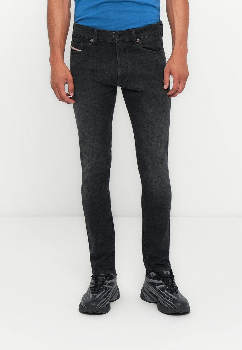 Schwarze Denim-Jeans mit schmaler Passform, ausgestattet mit Fronttaschen, Gürtelschlaufen und dezentem Branding. Kombiniert mit schwarzen Sportschuhen.