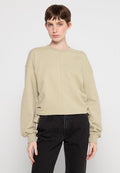 Beige verkürzter Pullover mit langen Ärmeln, gerippten Bündchen, seitlichen Raffungselementen und rundem Ausschnitt. Getragen mit schwarzen Hosen.