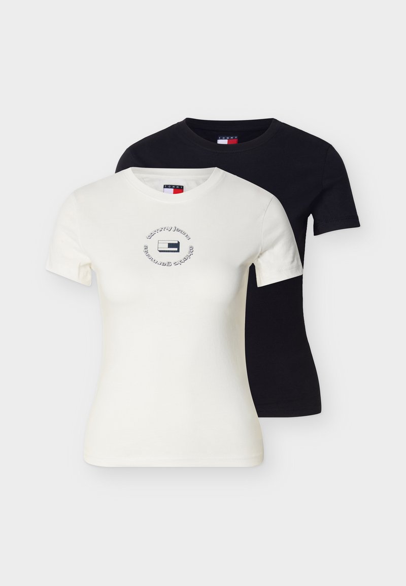 Weißes enganliegendes Kurzarm-T-Shirt mit rundem Tommy Jeans Logo auf der Brust, über einem schlichten schwarzen enganliegenden Kurzarm-T-Shirt getragen.
