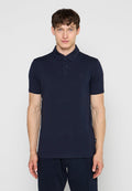 Mann trägt ein eng anliegendes dunkelblaues Poloshirt mit kurzen Ärmeln und geknöpftem Kragen, steht vor einem einfarbigen hellen Hintergrund.