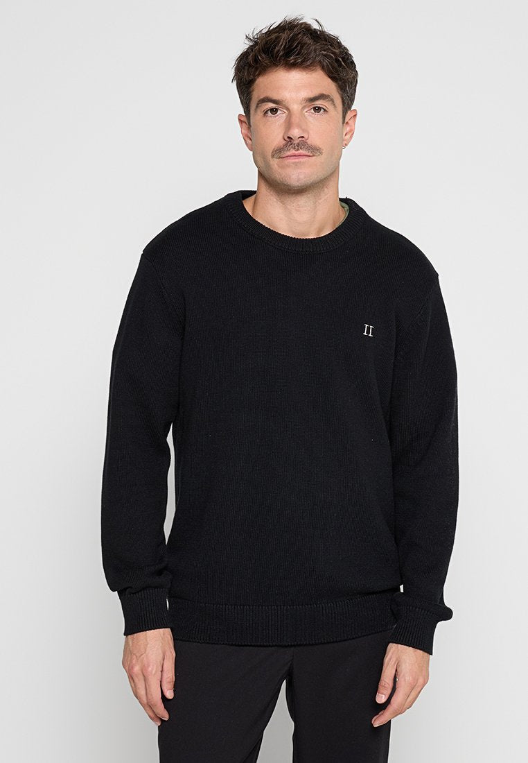 Schwarzer Strickpullover mit Rundhalsausschnitt, gerippten Bündchen und einem kleinen gestickten Design auf der Brust. Strukturiertes Material und lässige Passform.