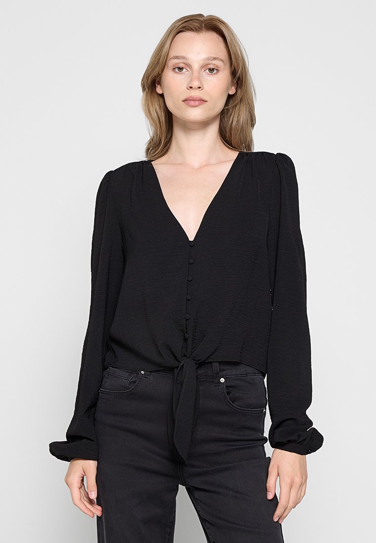 Schwarze Bluse mit langen Ärmeln, V-Ausschnitt, Knopfverschlüssen und einem gebundenen Vorderteil. Hergestellt aus strukturiertem Stoff mit lässiger Passform.