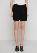 Schwarze, taillierte Shorts mit hoher Taille, die vordere Falten und einen Knopfverschluss aufweisen, aus strukturiertem Stoff gefertigt und kombiniert mit dunklen Slippern.