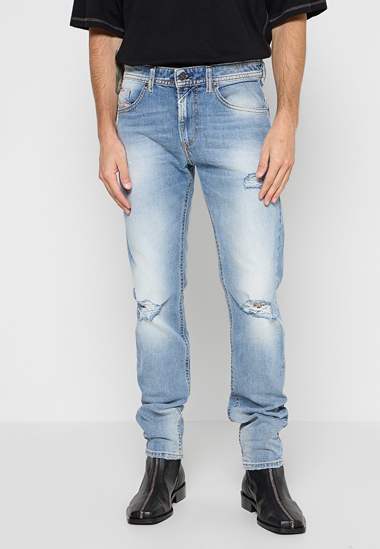 Hellblaue Denimjeans mit geradem Schnitt, die verwitterte Akzente, ein ausgewaschenes Muster und ein klassisches Fünf-Taschen-Design aufweisen. Getragen mit schwarzen Stiefeln.