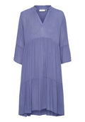 Luftiges, gestuftes Kleid aus helllila Stoff. Mit V-Ausschnitt, Dreiviertelärmeln und einer strukturierten Oberfläche.