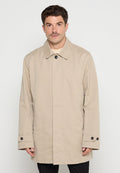 Mann in beige Knopfjacke mit Kragen, der vor einem schlichten weißen Hintergrund steht.