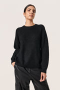 Schwarzer, gerippter Pullover mit runder Ausschnitt und überschnittenen Schultern, kombiniert mit schwarzer Lederhose, weich in der Textur und mit lässiger Passform.