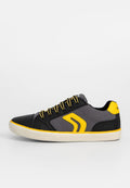 Schwarze und graue Sneaker mit gelben Akzenten, ausgestattet mit einem glatten Lederoberteil, strukturiertem Stoff an der Seite und kontrastierenden Schnürsenkeln. Flache Gummisohle.