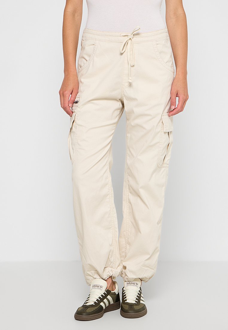 Beige Cargo-Hosen aus Baumwolle mit lockerer Passform, mit Kordelzugbund, Seitentaschen und elastischen Bündchen. Akzentuiert mit Cargo-Taschen.
