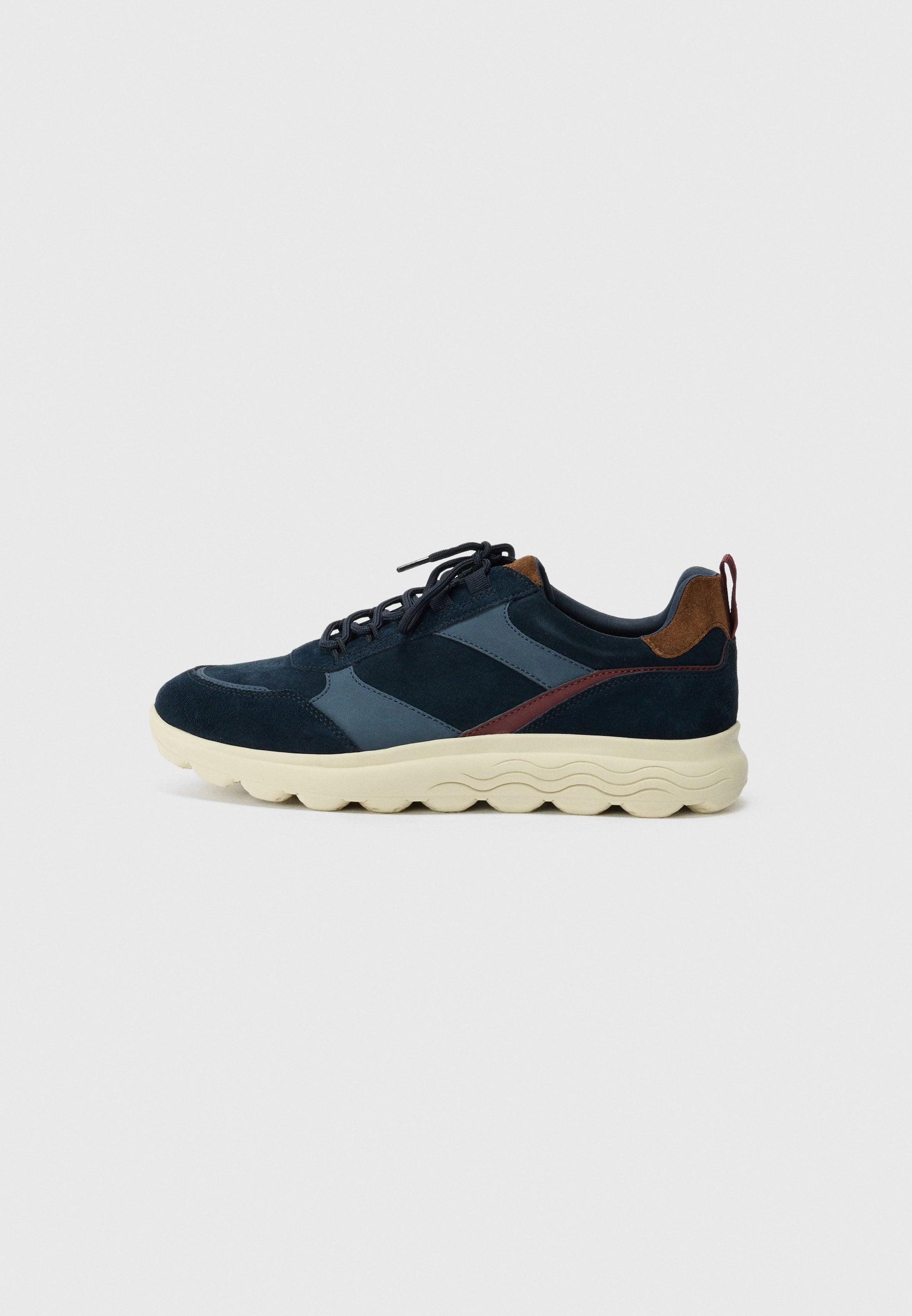 Marineblau und dunkelblaue Wildledersneaker mit einer beigen strukturierten Sohle, hervorhebenden braunen Lederelementen und schwarzen Schnürsenkeln. Seitliches Design-Detail.