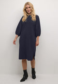 Marineblaues knielanges Kleid mit Puffärmeln, strukturiertem Stoff, seitlichem Schlitz und lockerer Passform. Getragen mit schwarzen Knöchelstiefeln.