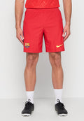 Mann trägt rote FC Barcelona Fußballshorts mit Vereinswappen und gelbem Nike-Logo, weiße Socken und schwarze Fußballschuhe, steht vor weißem Hintergrund.