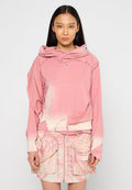 Helles rosa Übergröße-Hoodie mit abgerundetem Saum, ausgestattet mit einer Kängurutasche und einer geschichteten Kapuze. Kombiniert mit einem pastellfarbenen Tie-Dye-Reißverschlussrock mit Taschen.