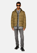 Olivgrüne Steppjacke mit Reißverschluss, getragen über einem grauen Denimhemd, kombiniert mit grauen Jeans und schwarzen Sneakers. Robuste, strukturierte Materialien.