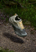 Leichtgewichtiger grauer Gore-Tex-Schuh mit einem strukturierten schwarzen Mesh-Bereich, gelben Schnürsenkeln und gepolsterten Sohlen, erhöht über einer Kiesoberfläche.