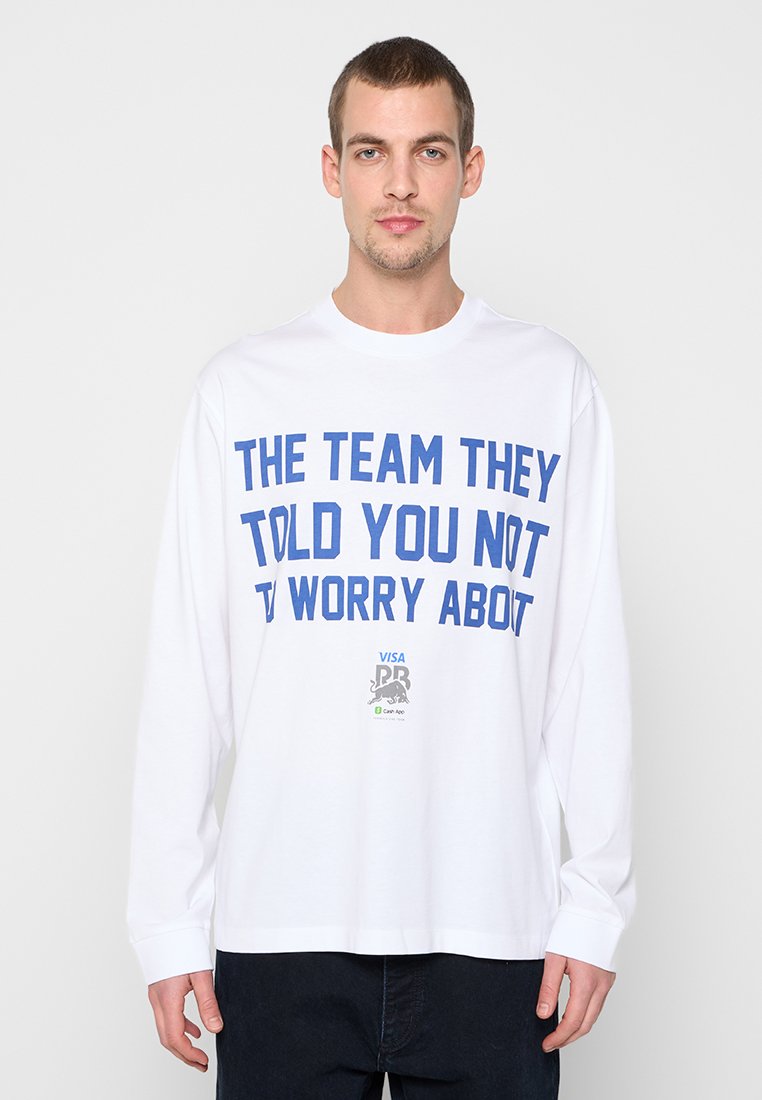 Weißes Langarm-T-Shirt mit blauem fettem Text "THE TEAM THEY TOLD YOU NOT TO WORRY ABOUT" und kleinen Logos auf der unteren Vorderseite.