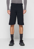 Mann trägt schwarze knielange Shorts, graues Langarmshirt, dunkelgraue Socken und schwarze Sportschuhe und steht vor einem schlichten Hintergrund.