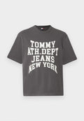 Graues Baumwoll-T-Shirt mit kurzen Ärmeln, mit fettem weißen Text: "TOMMY ATH.DEPT JEANS NEW YORK" in einem gewölbten Design.