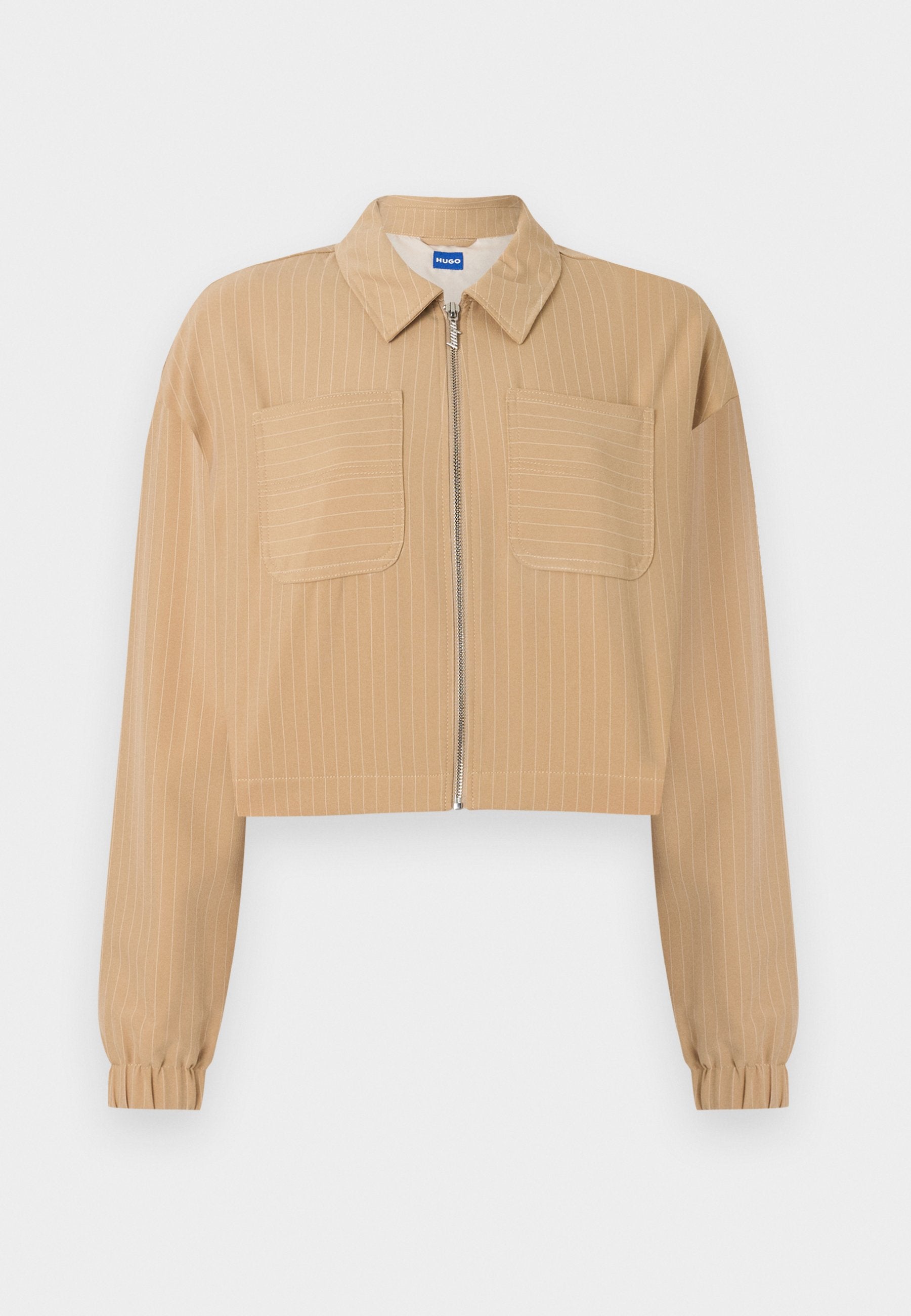 Beige verkürzte Jacke mit dünnen weißen Nadelstreifen, Reißverschluss vorne, zwei Brusttaschen, langen Ärmeln mit elastischen Bündchen und spitzem Kragen.