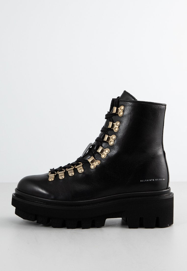 Schwarze Leder-Stiefelette mit goldenen Hardware-Akzenten und runder Zehenpartie. Verfügt über eine dicke, robuste Sohle und gestickte Details an den Seiten.