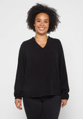 Schwarze Bluse mit langen Ärmeln und V-Ausschnitt, aus softem Stoff gefertigt, mit geraffter Naht entlang des Ausschnitts. Kombiniert mit dunklen Jeans.