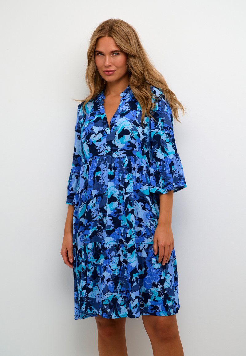 Blaues Blümchenkleid mit V-Ausschnitt, gestuftem Design und 3/4-Ärmeln mit Glockenform. Es weist verschiedene Blautöne in abstrakten Mustern auf und hat eine fließende Silhouette.