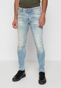 Faded blaue Skinny-Jeans aus Denim, mit abgenutzten Details und Farbspritzern, kombiniert mit schwarzen Turnschuhen.