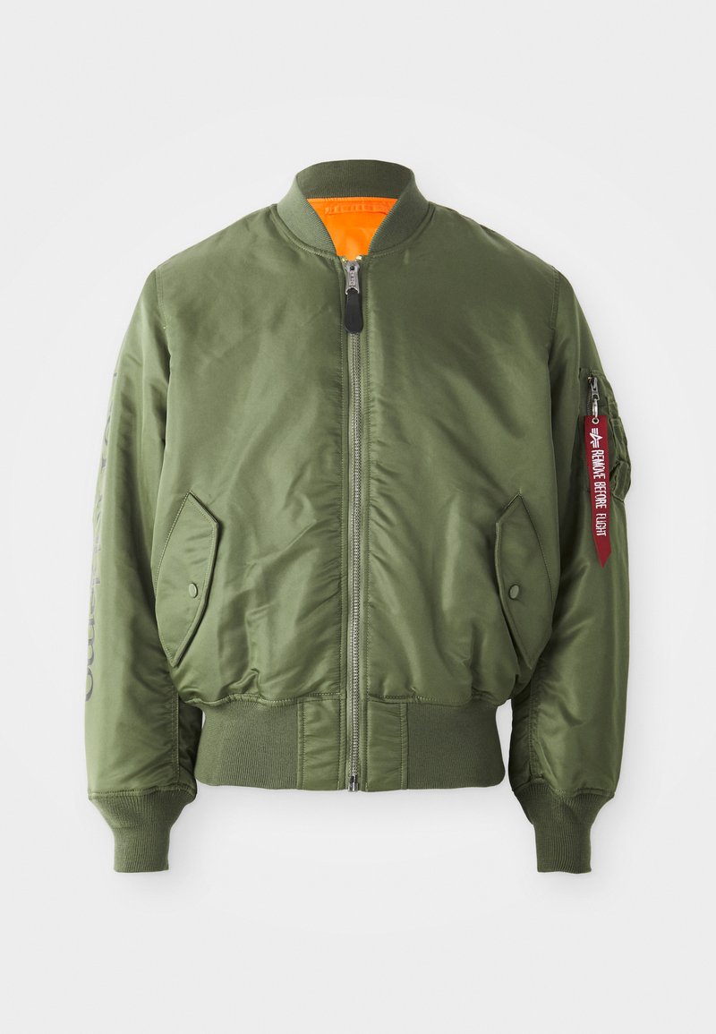 Olivgrüne Bomberjacke mit Reißverschluss vorne, gerippten Bündchen und Saum, Seitentaschen und orangefarbenem Futter. Mit rotem Etikett-Detail am Ärmel.