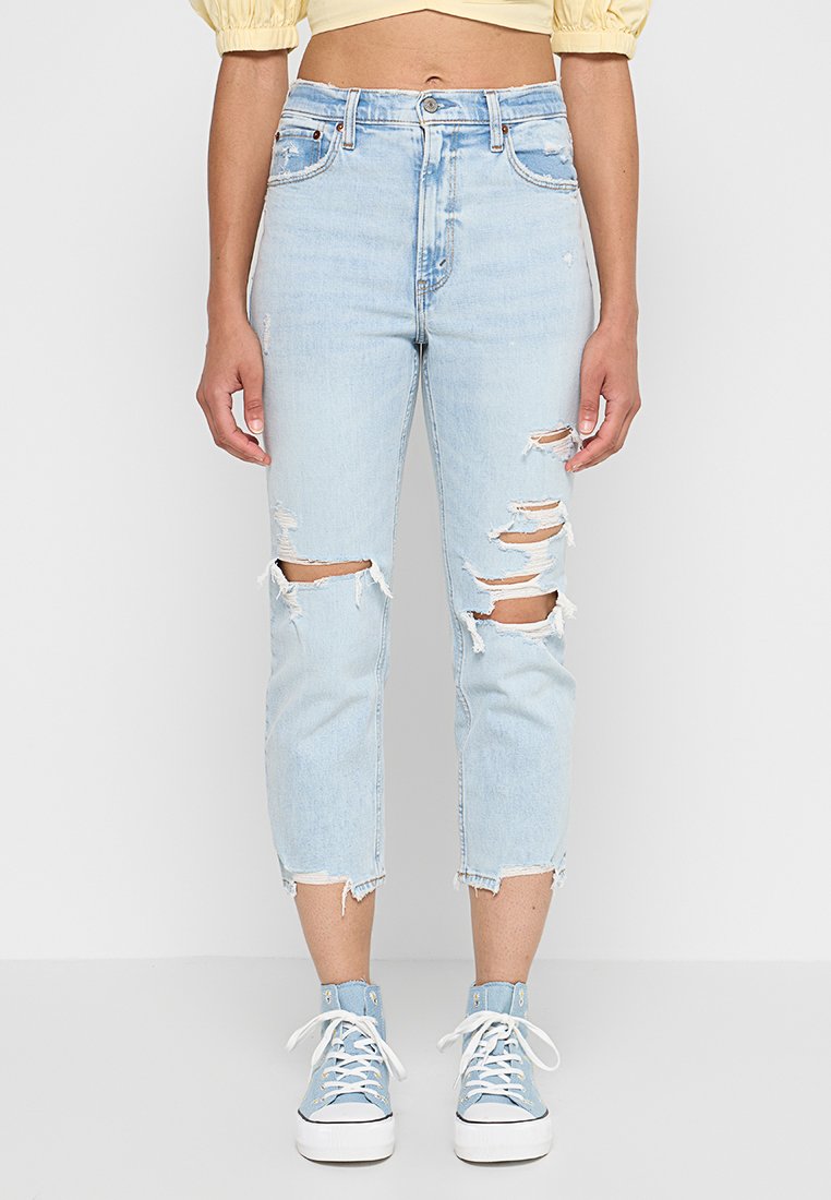 Hellblaue Jeans mit zerstörten Knien, ausgefranstem Saum und lockerer Passform. Kombiniert mit hellblauen High-Top-Sneakern.
