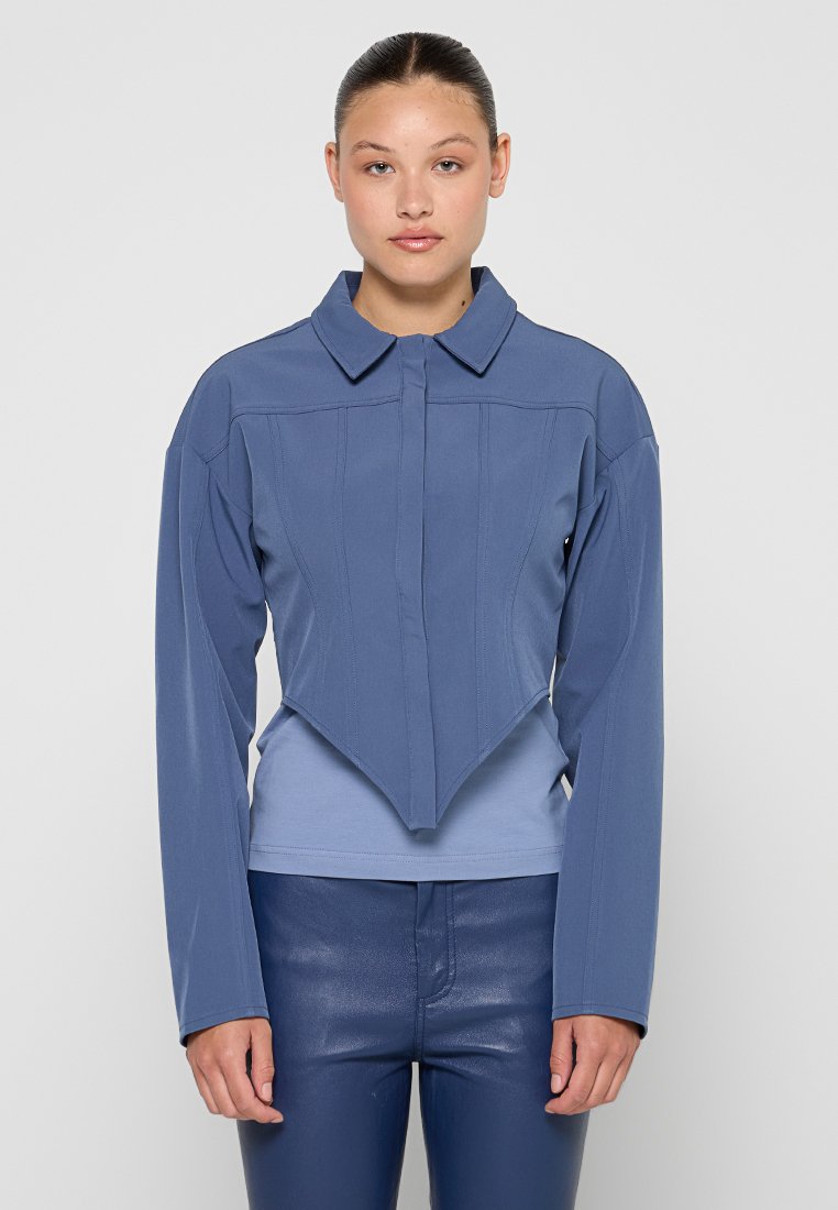 Blaue cropped Jacke mit strukturiertem Kragen, langen Ärmeln und einzigartigem, schrägen Saum; glattes Material mit dezenten Stichdetails.