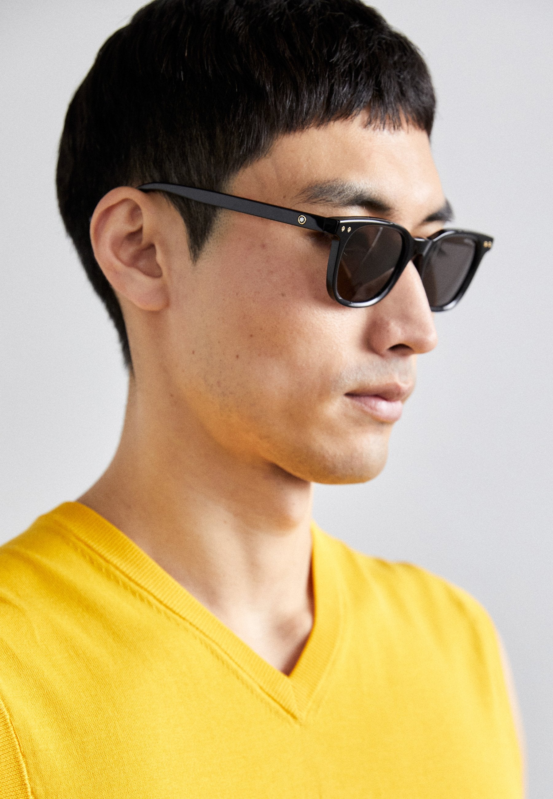 Sonnenbrille mit schwarzen Rahmen und dunklen Gläsern. Bemerkenswerte Details sind kleine goldene Akzente an den Scharnieren und eine rechteckige Form.
