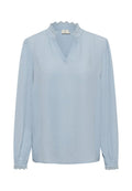 Hellblaue Bluse mit einem strukturierten Polka-Dot-Muster, V-Ausschnitt und Spitzenbesatz am Kragen und an den Manschetten. Lange Ärmel, lockere Passform.