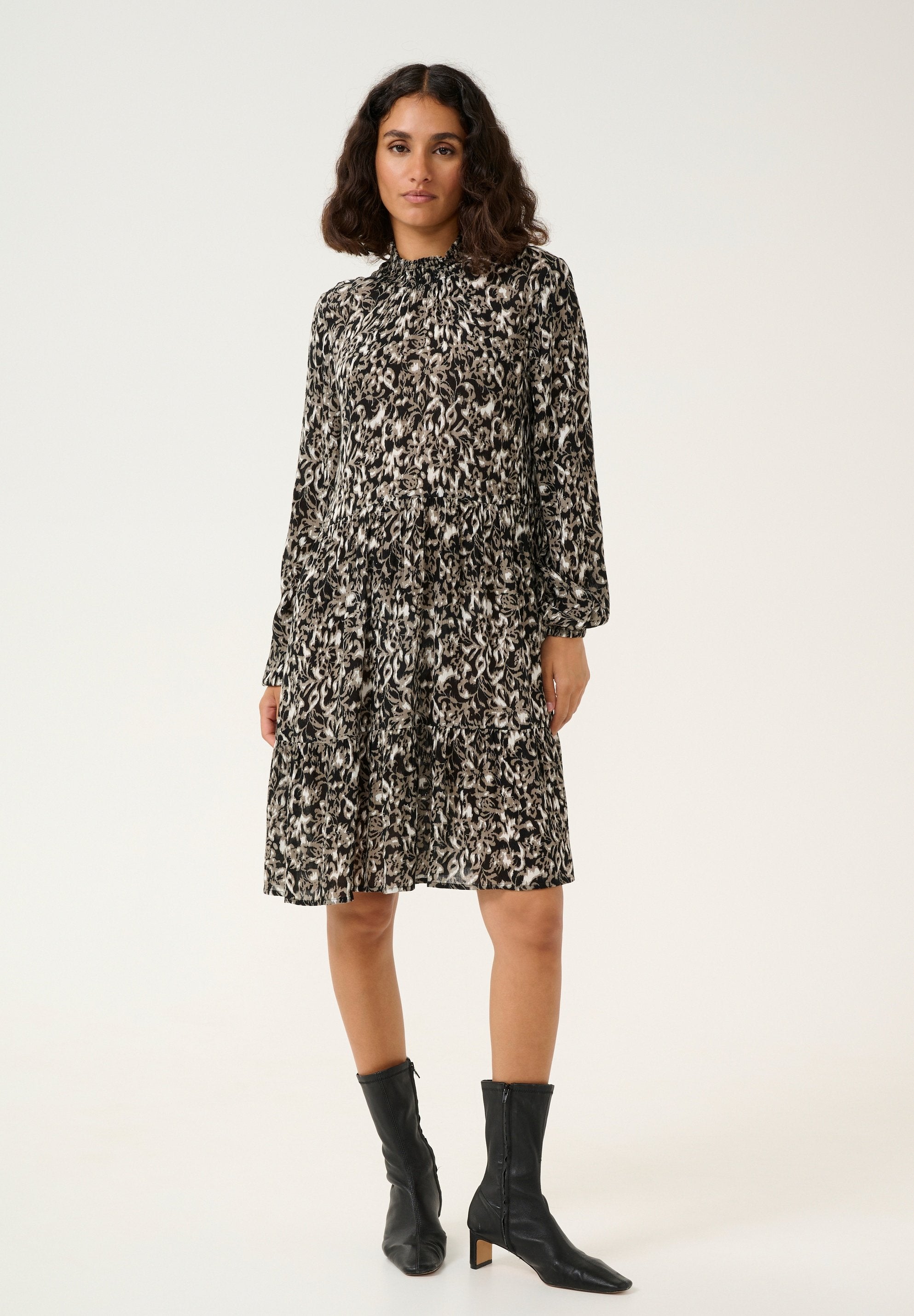 Schwarz- mit Cremefarben gemustertes Kleid mit langen Ärmeln, gesammeltem Bund, gestuftem Rock und hohem Ausschnitt, kombiniert mit schwarzen Knöchelstiefeln.