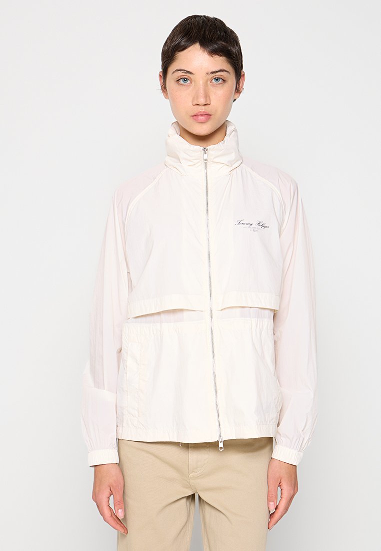 Leichte, cremefarbene Jacke mit hohem Kragen, Frontreißverschluss und seitlichen Taschen. Verfügt über ein cropped Design und ein Logodetail.
