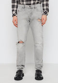 Helle graue Jeans aus Denim mit ausgefransten Kniedetails. Enganliegendes Design, Fünf-Taschen-Stil, abgenutzte Textur, kombiniert mit schwarzen Nieten-Schuhen.