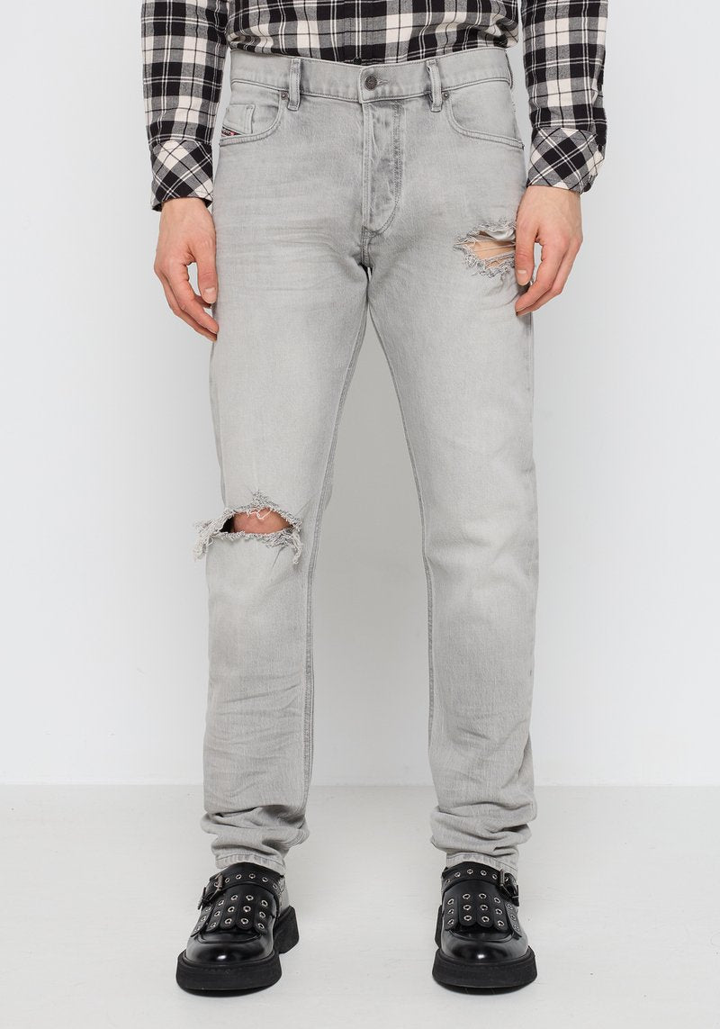 Helle graue Jeans aus Denim mit ausgefransten Kniedetails. Enganliegendes Design, Fünf-Taschen-Stil, abgenutzte Textur, kombiniert mit schwarzen Nieten-Schuhen.