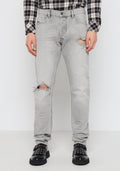 Helle graue Jeans aus Denim mit ausgefransten Kniedetails. Enganliegendes Design, Fünf-Taschen-Stil, abgenutzte Textur, kombiniert mit schwarzen Nieten-Schuhen.