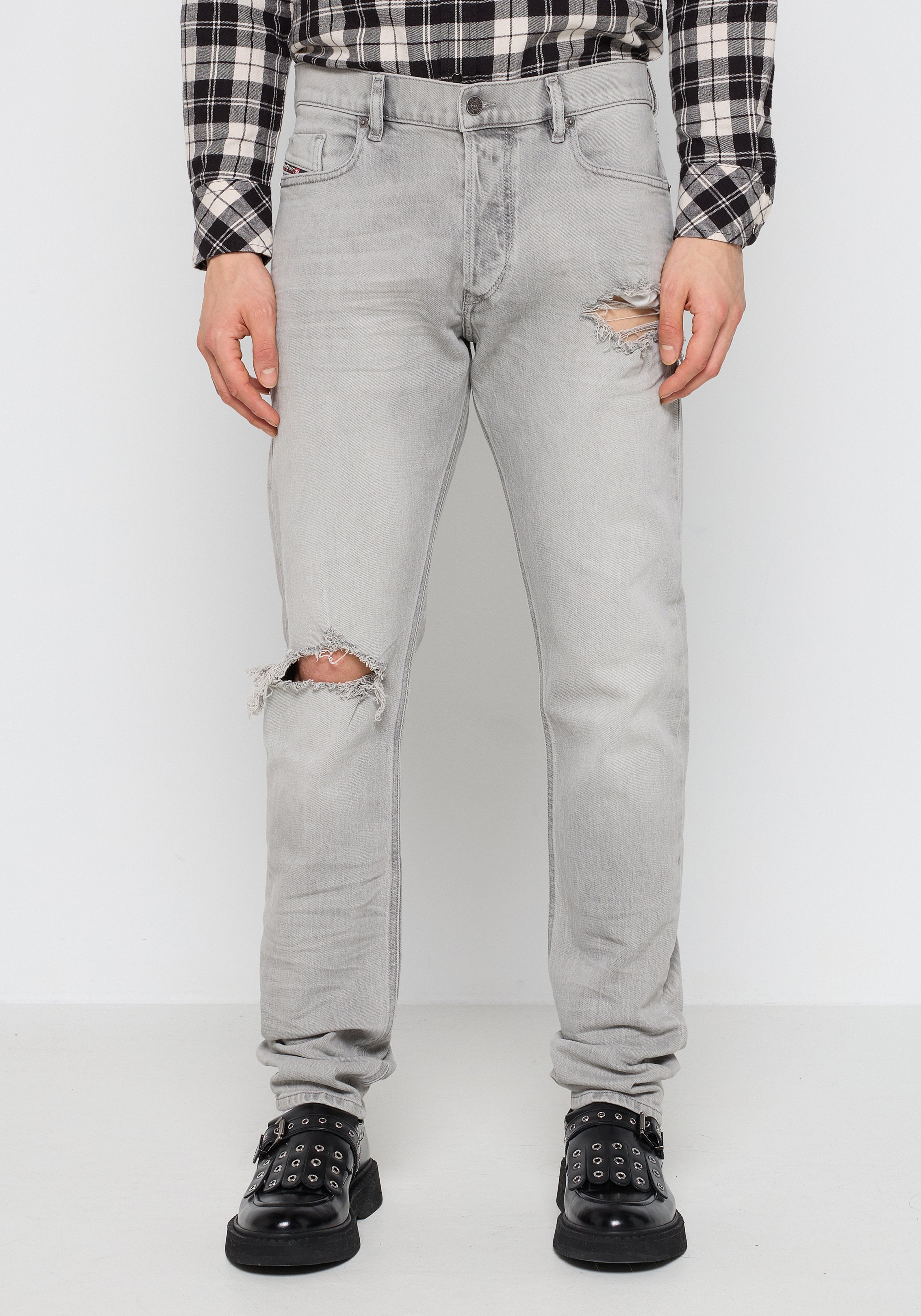 Helle graue Jeans aus Denim mit ausgefransten Kniedetails. Enganliegendes Design, Fünf-Taschen-Stil, abgenutzte Textur, kombiniert mit schwarzen Nieten-Schuhen.