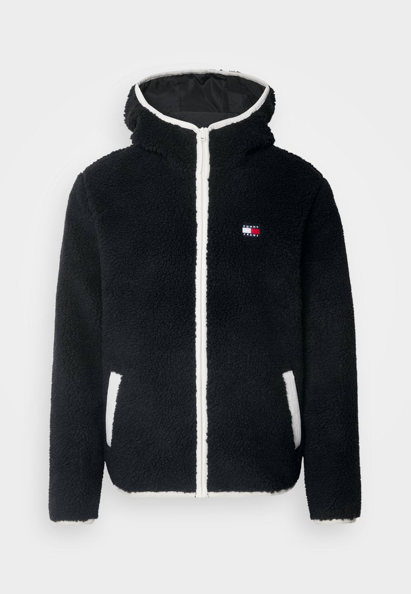 Schwarze Fleecejacke mit Kapuze, ausgestattet mit einem weißen Reißverschluss und Taschen; kleines Logo in Rot, Weiß und Blau auf der linken Brust. Weicher Stoff.